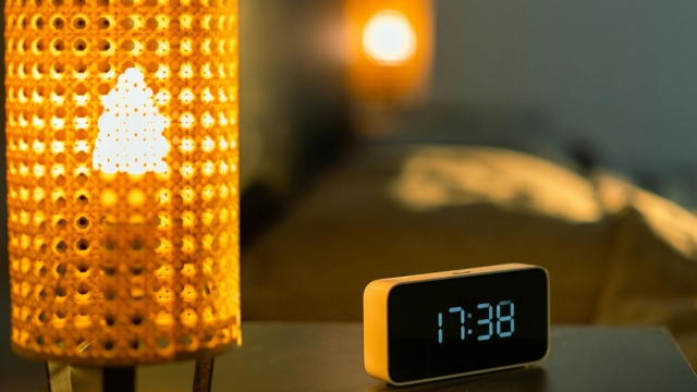 Noćna lampa sa toplim svetlom i digitalni sat na noćnom stočiću u modernoj spavaćoj sobi